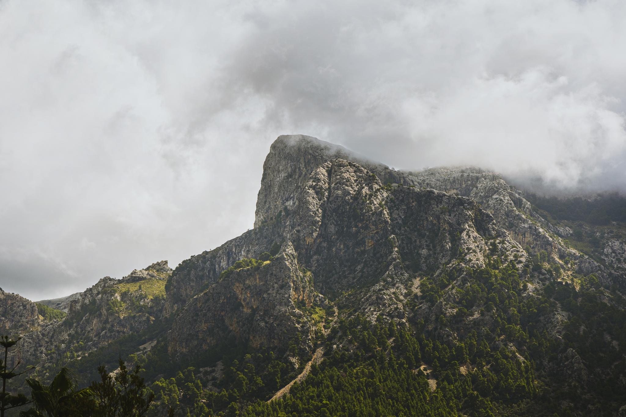 Can Gaspar, Balearic Islands, Spain — Dramatic limestone peak shrouded in mist, forested slopes, moody sky, Mediterranean mountain landscape