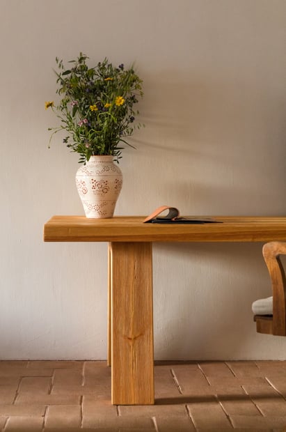 São Lourenço do Barrocal, Portugal — Wooden console table with ceramic vase of wildflowers and sunlight casting shadows on terracotta floor.