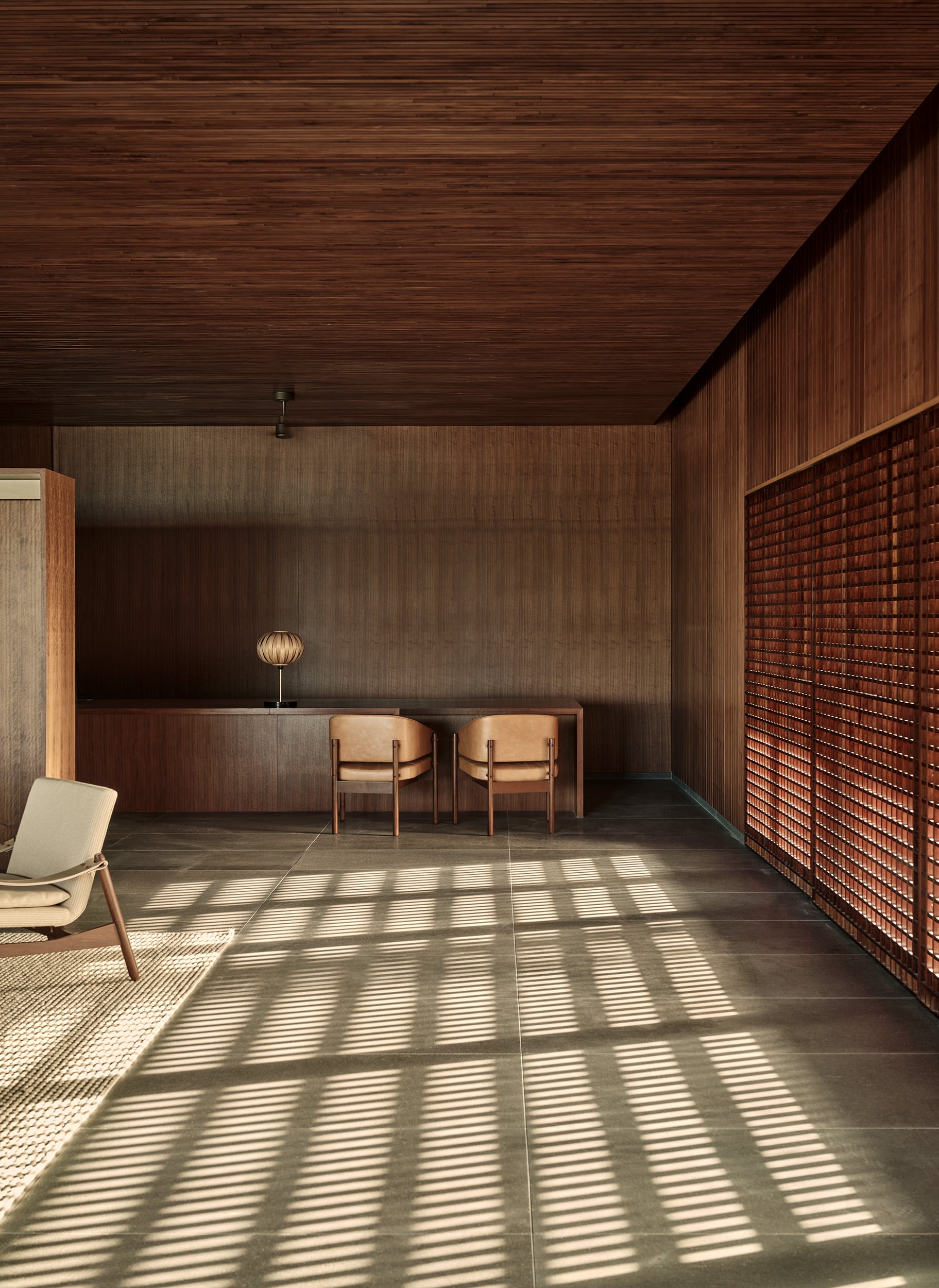 Patina Maldives, Asia — Minimalist wooden interior with leather chairs, geometric light patterns through brick screen, warm earth tones and natural materials.