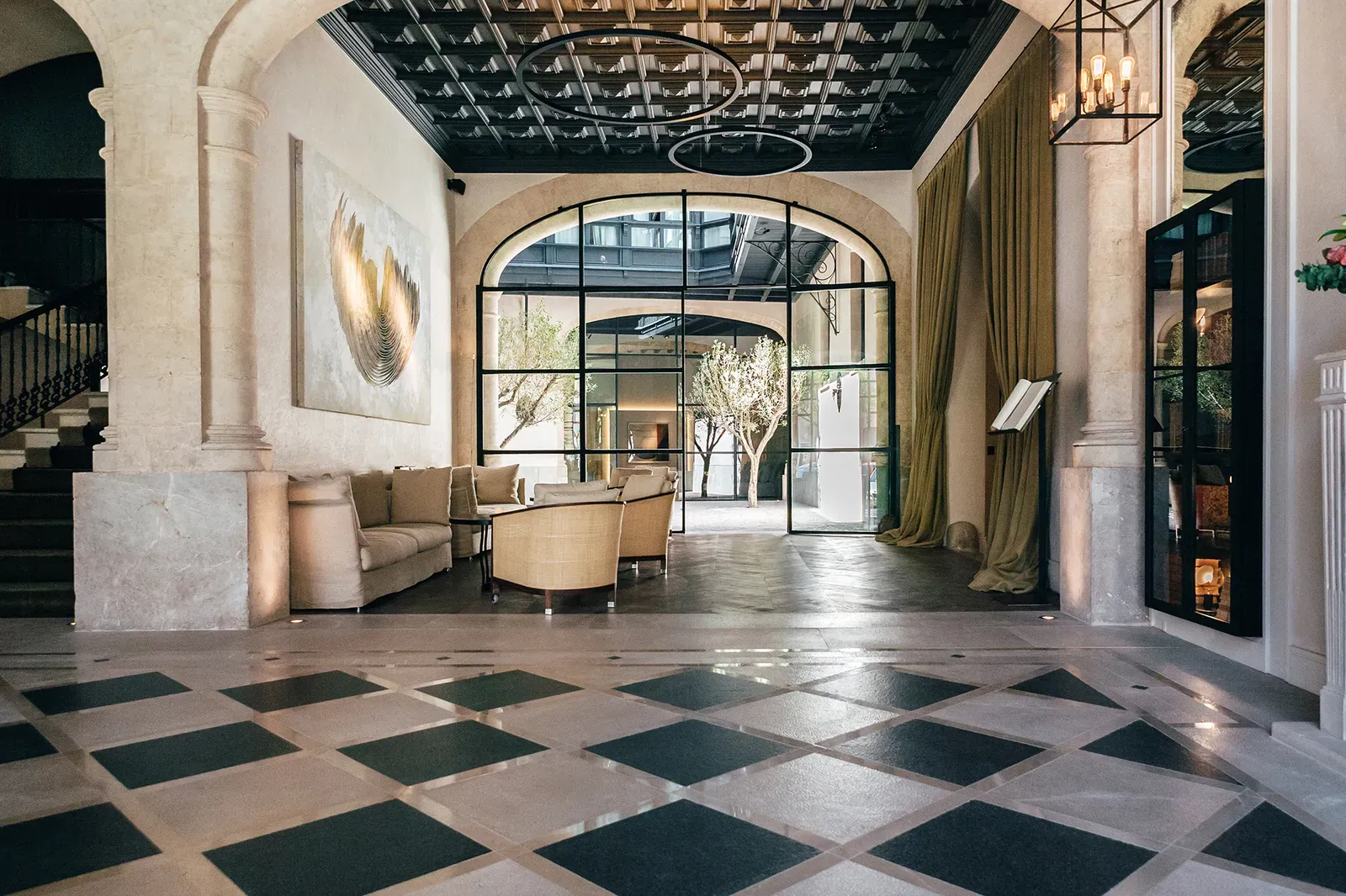Sant Francesc Hotel Singular, Balearic Islands, Spain — Arched windows frame courtyard greenery in luminous lobby with diamond-patterned marble floors and curved seating.