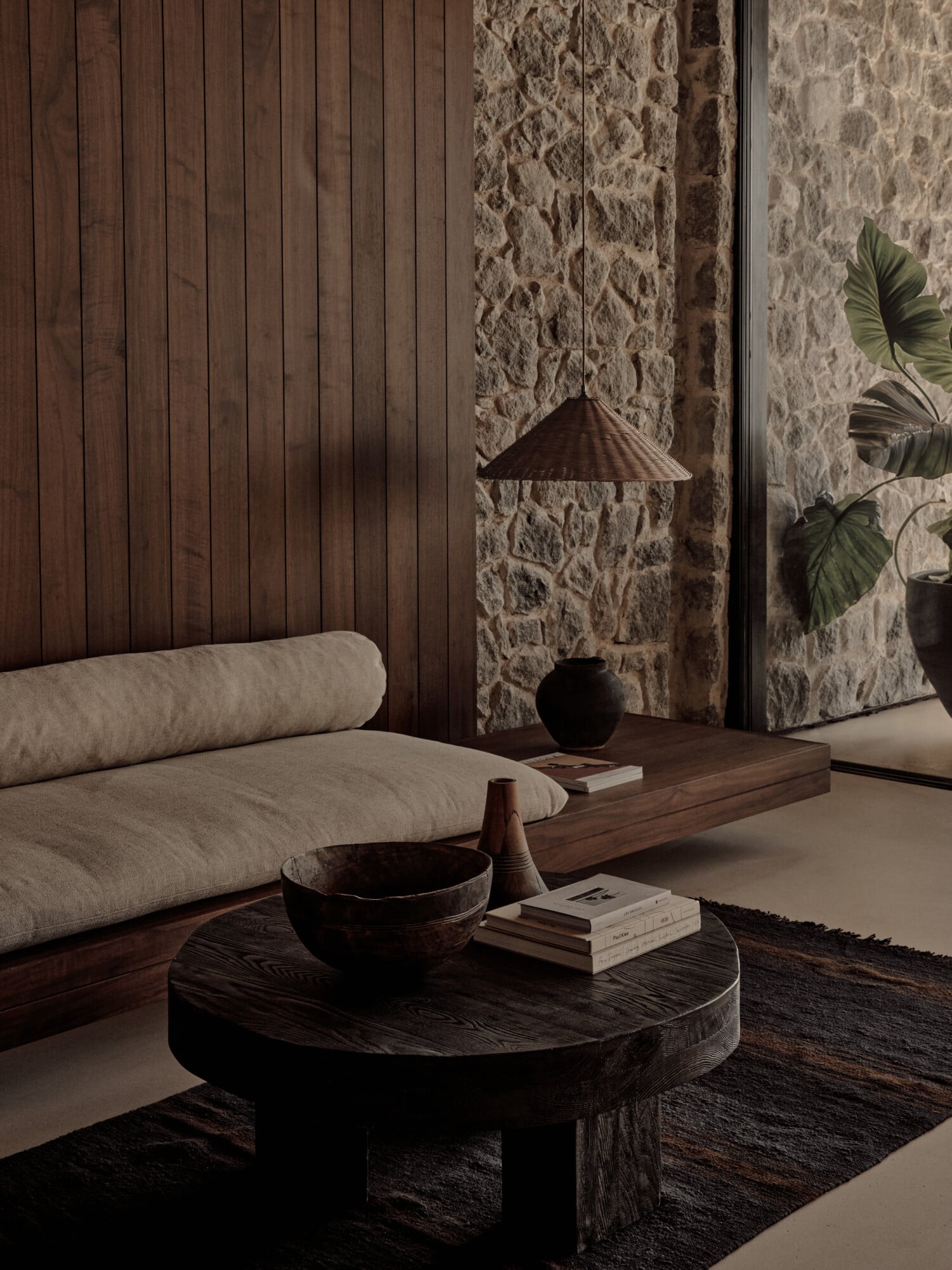 Minimalist lounge at Scorpios Bodrum with stone walls, wooden pendant lamp, and low platform seating in neutral textiles.