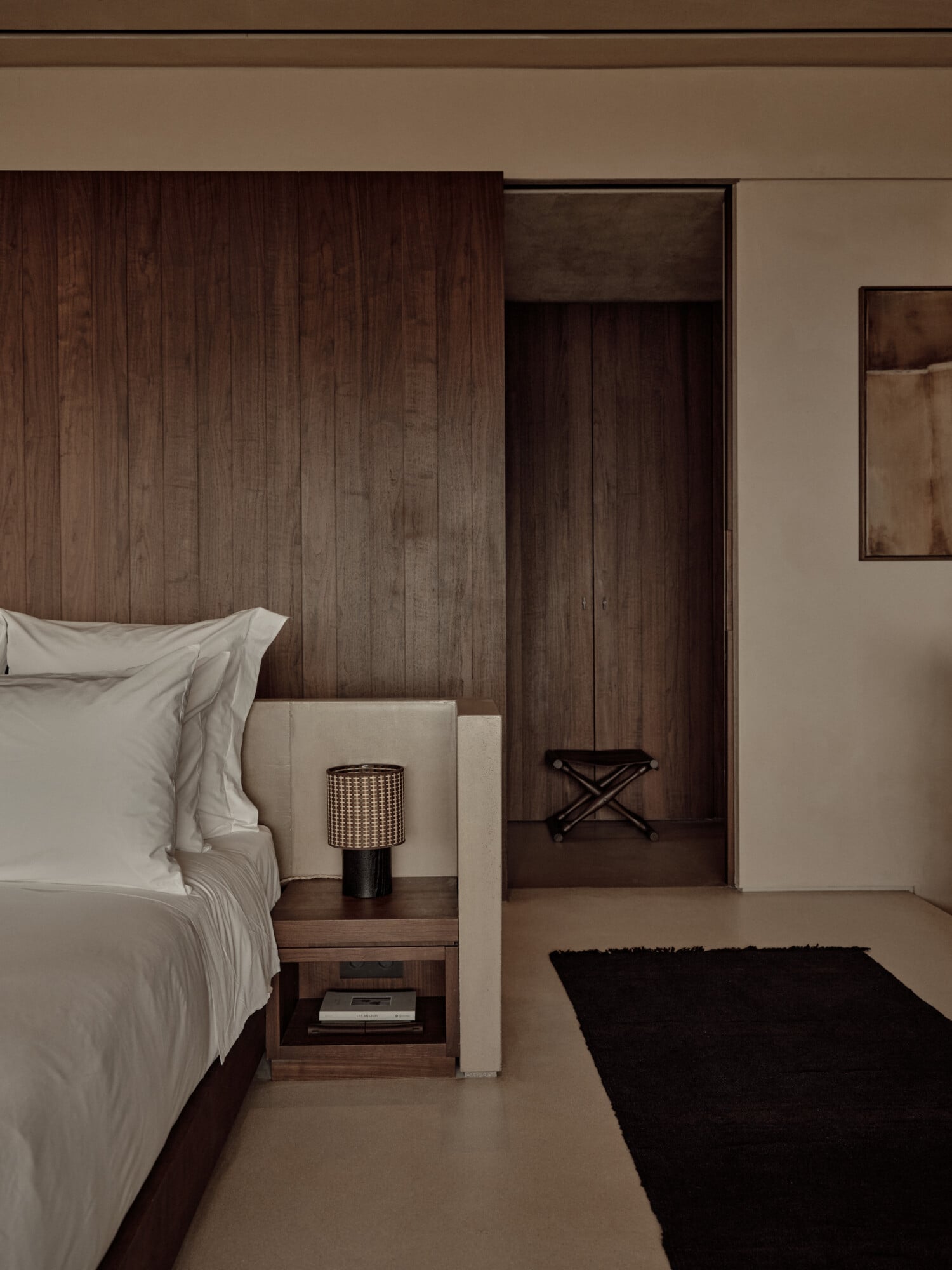 Scorpios Bodrum, Mediterranean — Minimalist bedroom with dark wood headboard, cream linens, woven pendant lamp, and open dressing alcove in neutral tones.