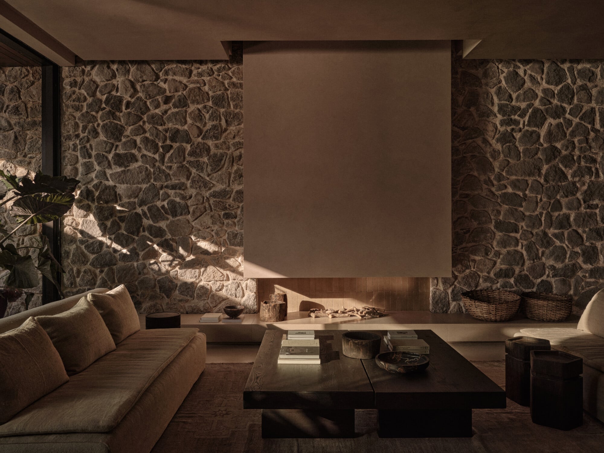 Scorpios Bodrum, Mediterranean — Minimalist lounge with stone walls, warm lighting, linen sofa, dark wood table, and neutral earth-tone palette creating serene luxury hospitality interior.