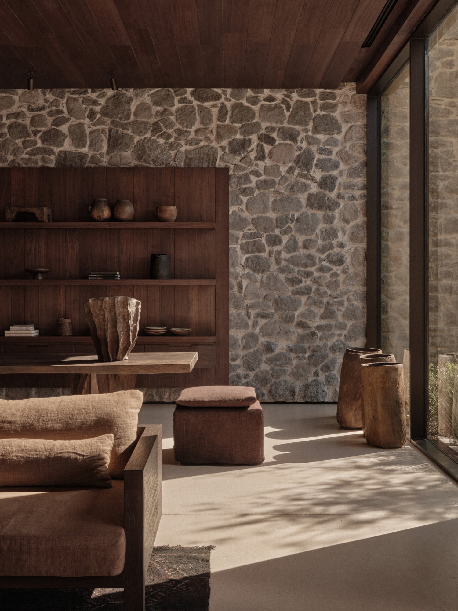 Scorpios Bodrum, Mediterranean — Stone wall interior with wooden shelving, linen seating, and natural light casting shadows across neutral floor.