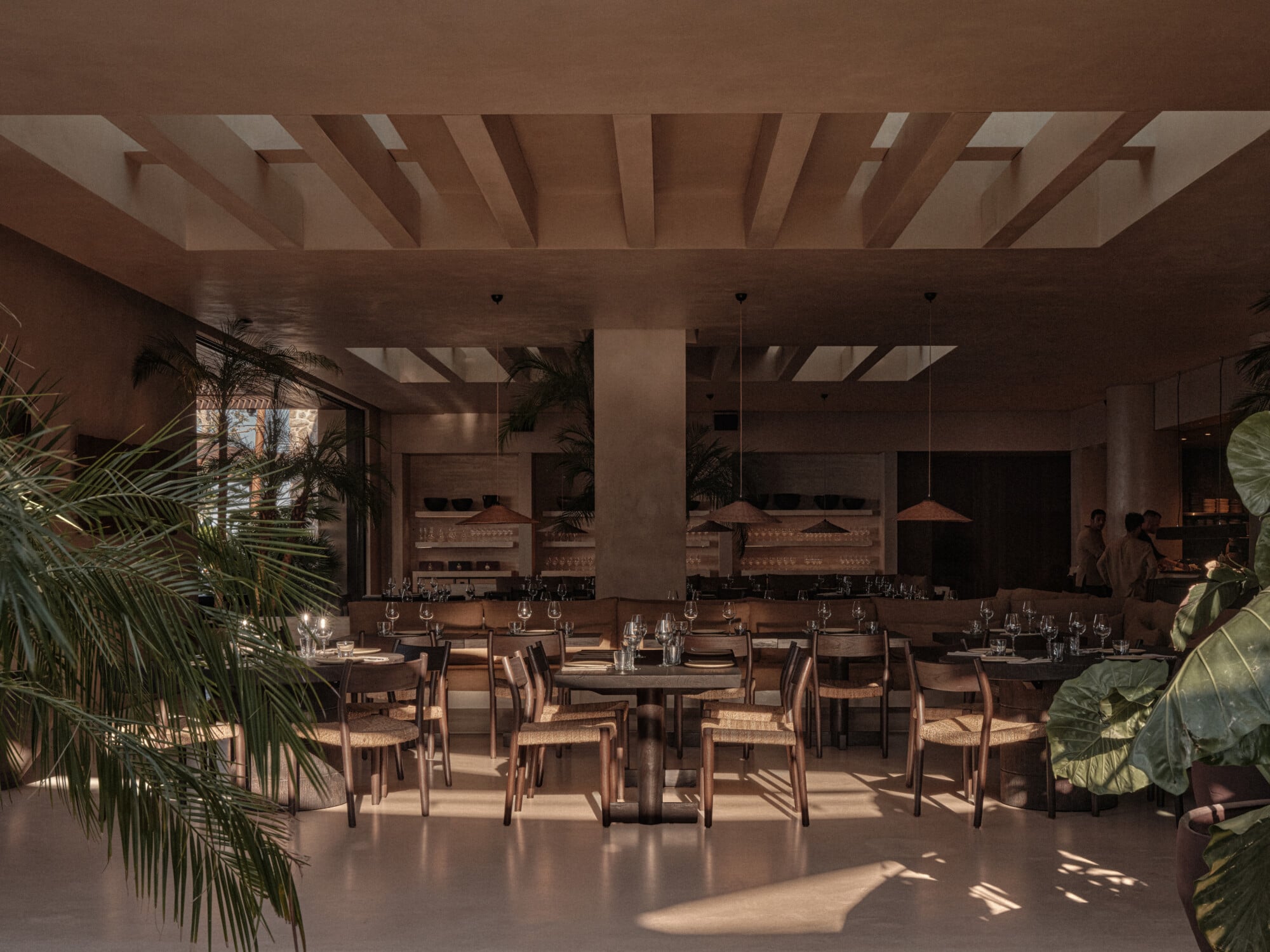 Scorpios Bodrum, Mediterranean — Sunlit dining room with wooden beam ceiling, woven chairs, potted palms, pendant lights, and expansive windows overlooking terracotta rooftops.
