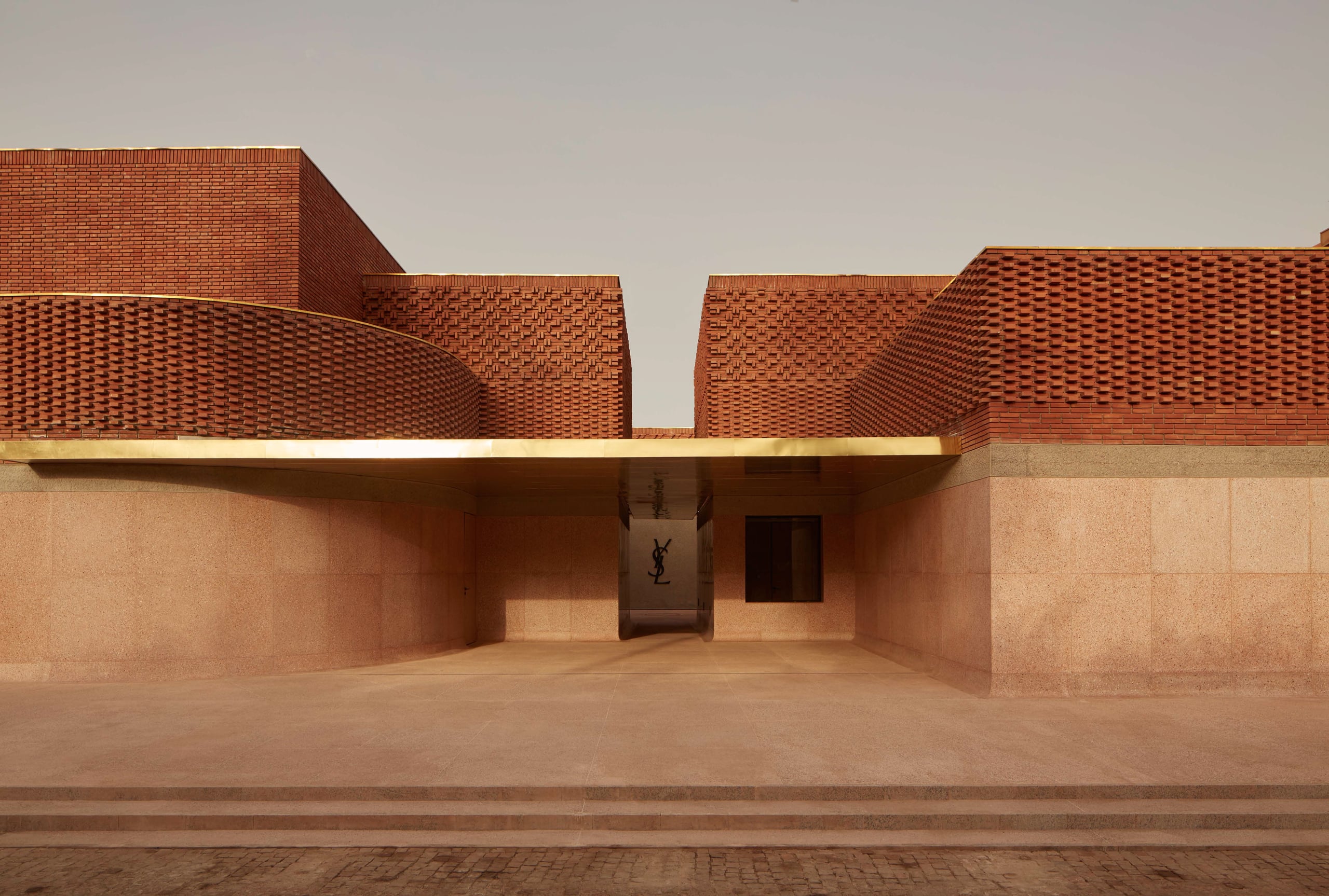 Musée Yves Saint Laurent | Marrakech, Morocco — Musée Yves Saint Laurent, Marrakech, Morocco — Modernist courtyard with terracotta brick pavilions, geometric perforated facades, and sculptural rooflines casting sharp shadows under bright daylight.