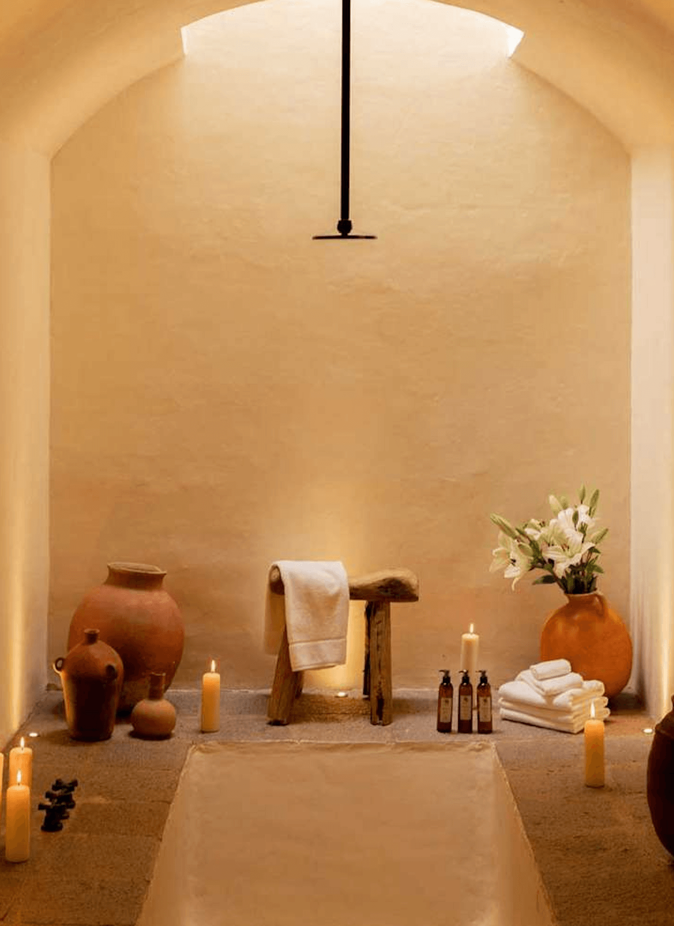La Valise San Miguel, Mexico — Spa alcove with terracotta vessels, wooden towel rack, white flowers, candles, and stone basin beneath arched ceiling with pendant light.