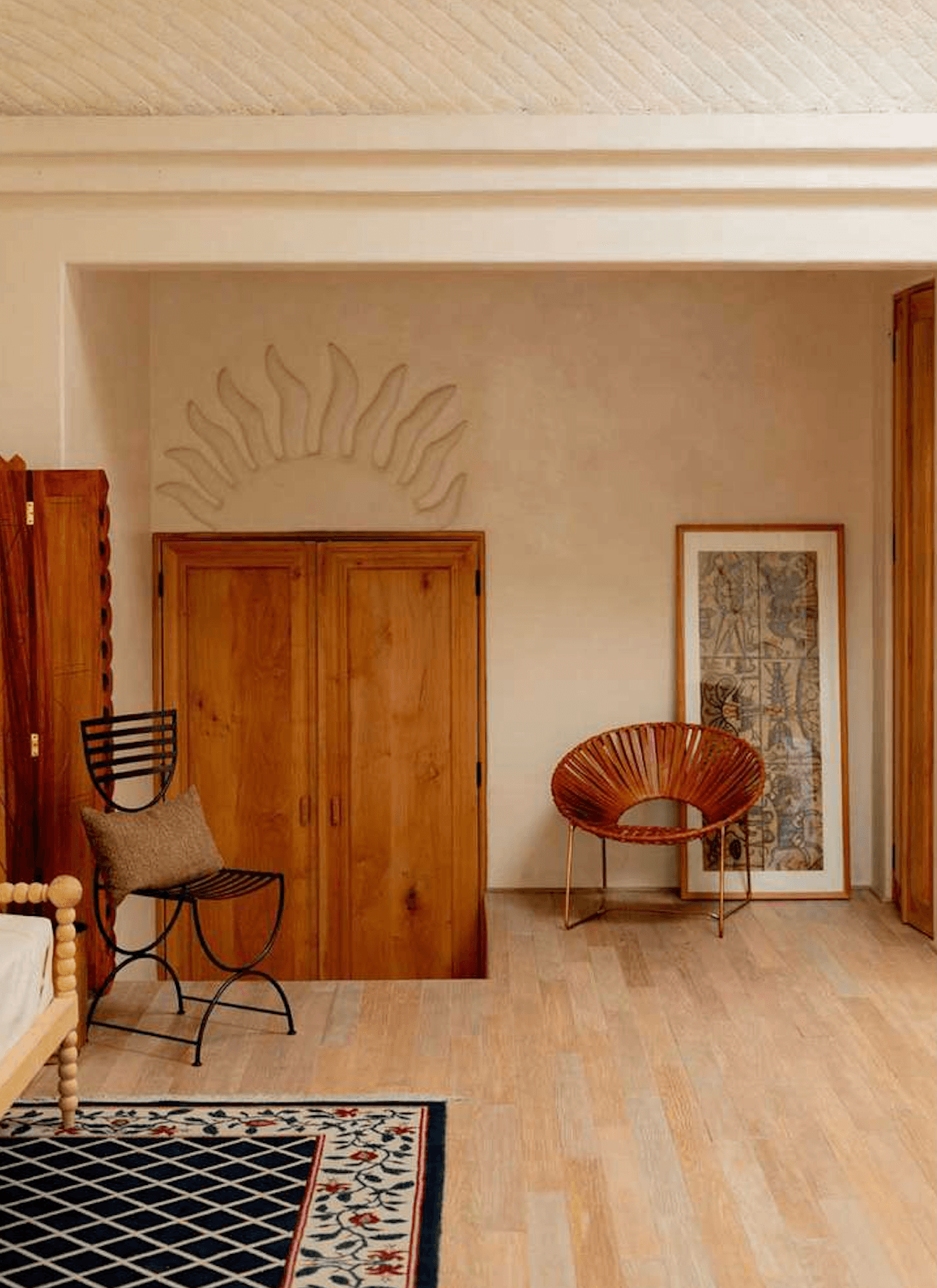 La Valise San Miguel, Mexico — Minimalist bedroom with terracotta wooden wardrobe, curved woven chair, sun relief wall art, geometric rug, natural light.