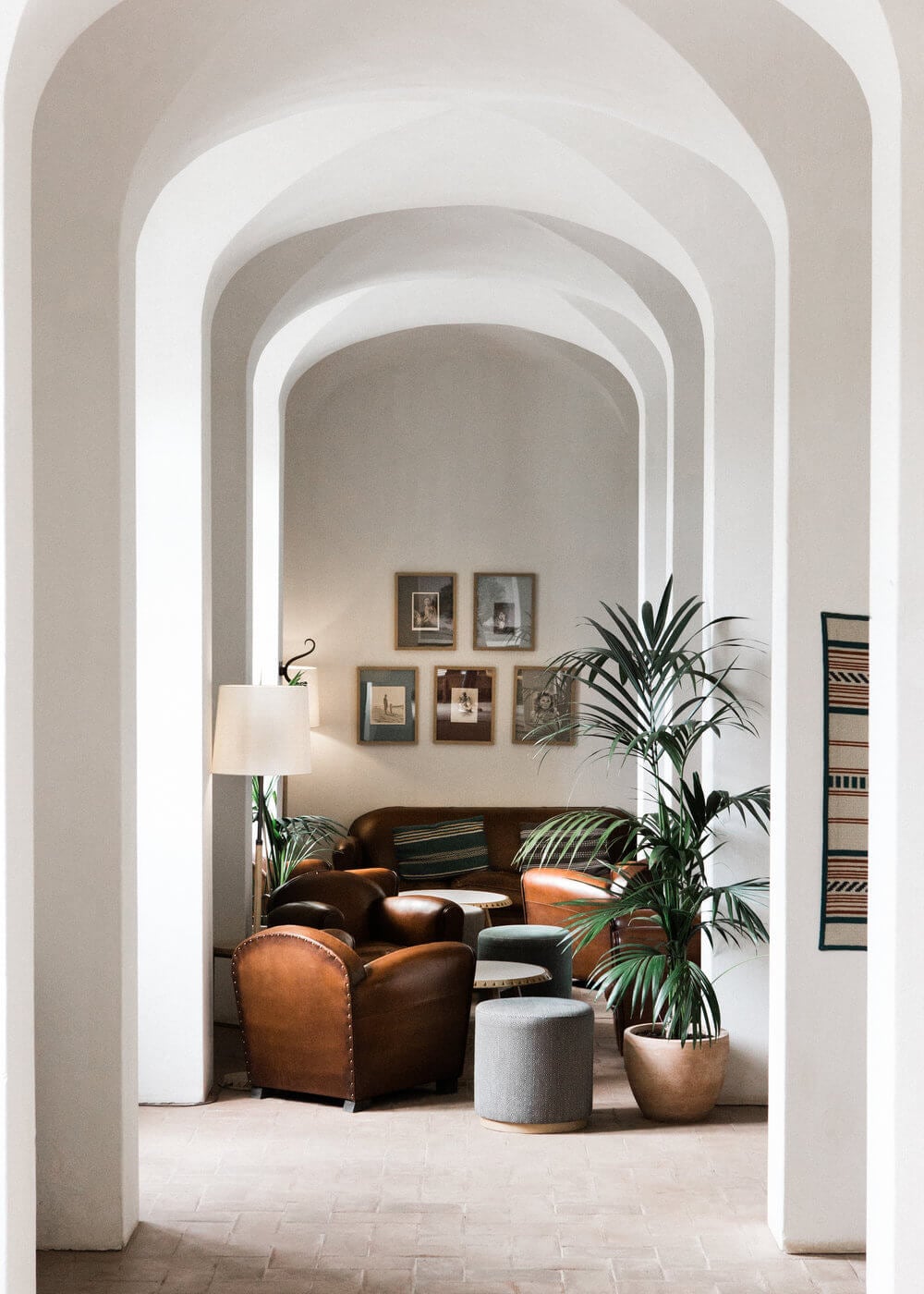 São Lourenço do Barrocal, Portugal — Arched corridor with cognac leather armchairs, potted palms, and framed artwork in minimalist Mediterranean interiors.