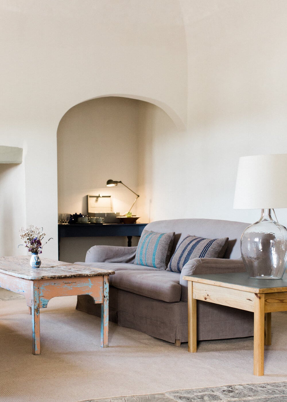 São Lourenço do Barrocal, Portugal — Arched stone alcove with desk and task lighting above linen sofa with striped pillows, rustic side tables, and soft natural light in minimalist whitewashed room.