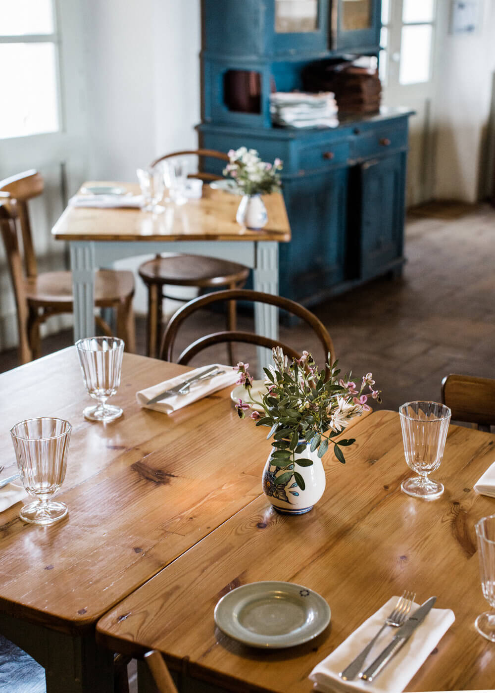 São Lourenço do Barrocal, Portugal — Wooden dining table with white ceramic vase, wildflowers, place settings, and vintage blue furniture in minimalist interior.