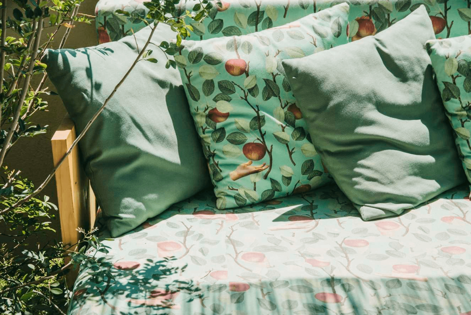 Casa Bonay, Europe — Outdoor bed with botanical bedding, apple-patterned pillows, linen cushions, and dappled sunlight through garden foliage.