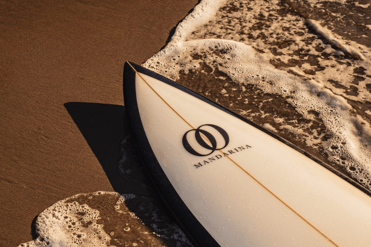 One&Only Mandarina, Mexico — Mandarina surfboard resting on sand with ocean waves, luxury resort lifestyle and coastal design aesthetic.