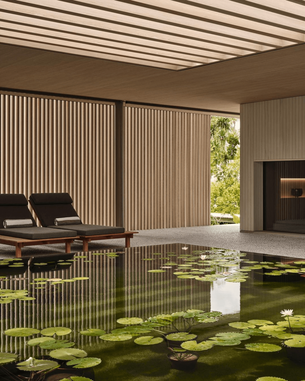 Flow Spa, Asia — Minimalist spa interior with indoor reflecting pool, lily pads, lounge chairs, slatted wood walls, and skylight in calm neutral tones.