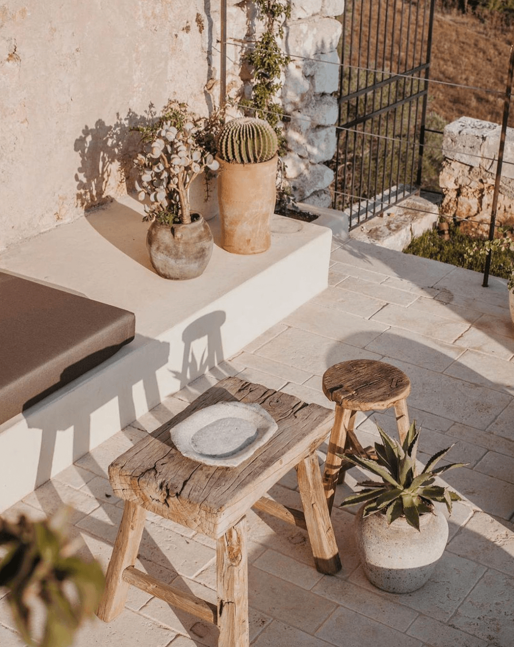 Dimora delle Balze, Europe — Rustic wooden table and stool with ceramic plate and potted cactus on sun-drenched terrace, whitewashed walls and stone courtyard.