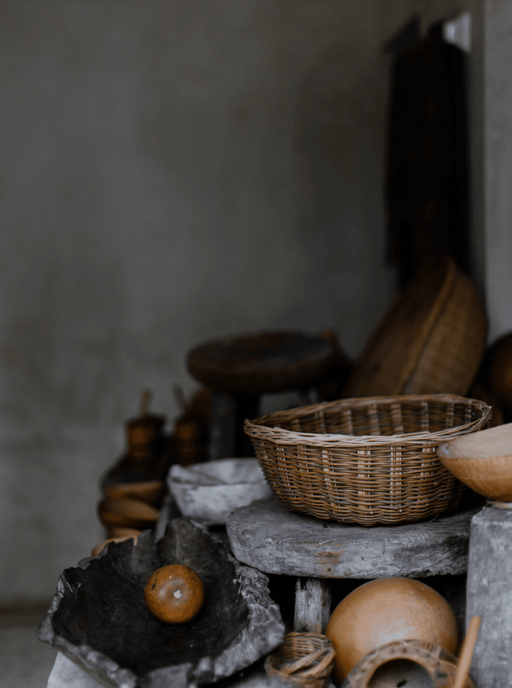Coqui Coqui Papholchac, Mexico — Woven basket and wooden vessels arranged on weathered stone shelf against neutral wall, artisanal still life.