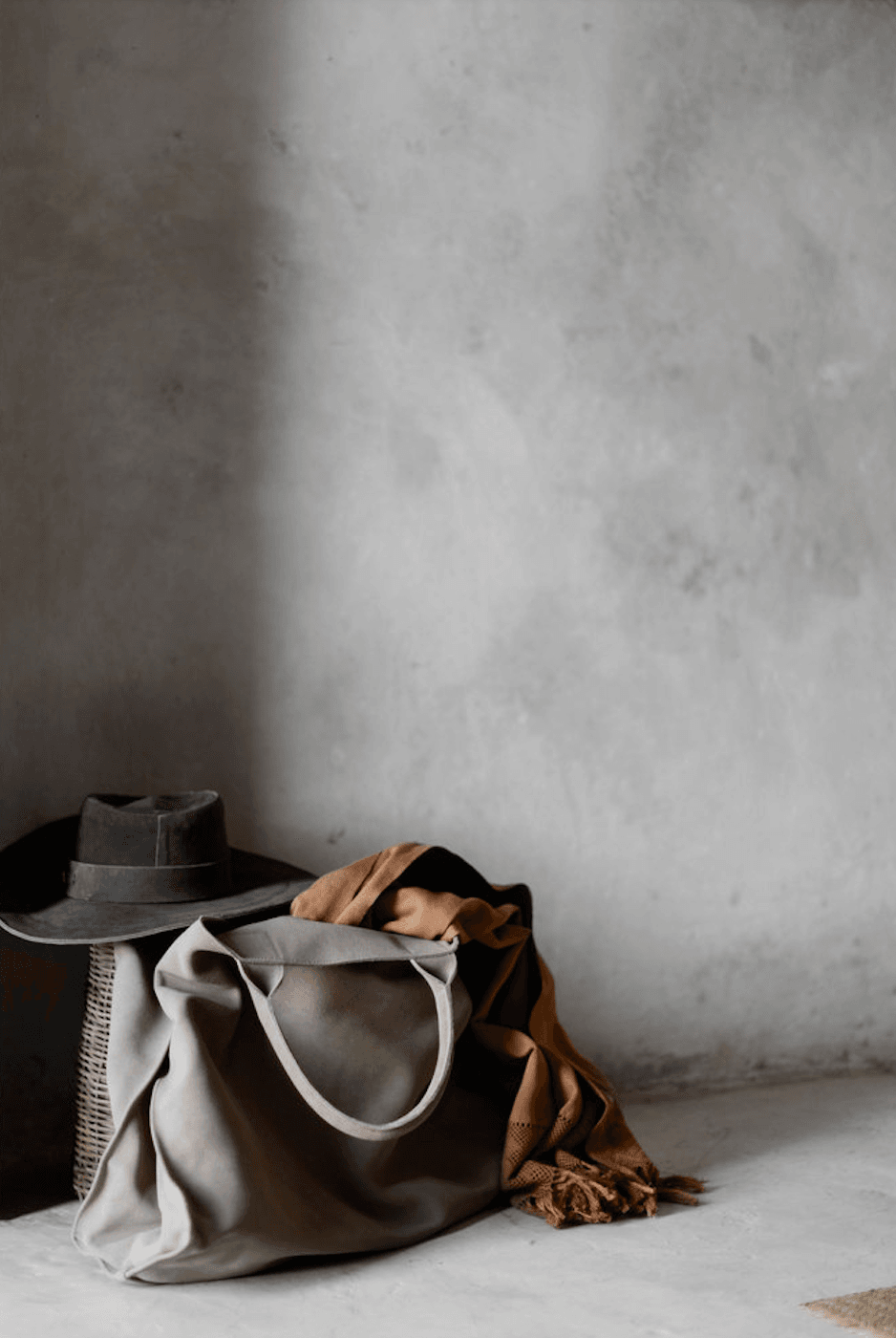 Coqui Coqui Papholchac, Mexico — Neutral linen tote bag with leather handles, black felt hat, and camel throw arranged against textured concrete wall with natural light.