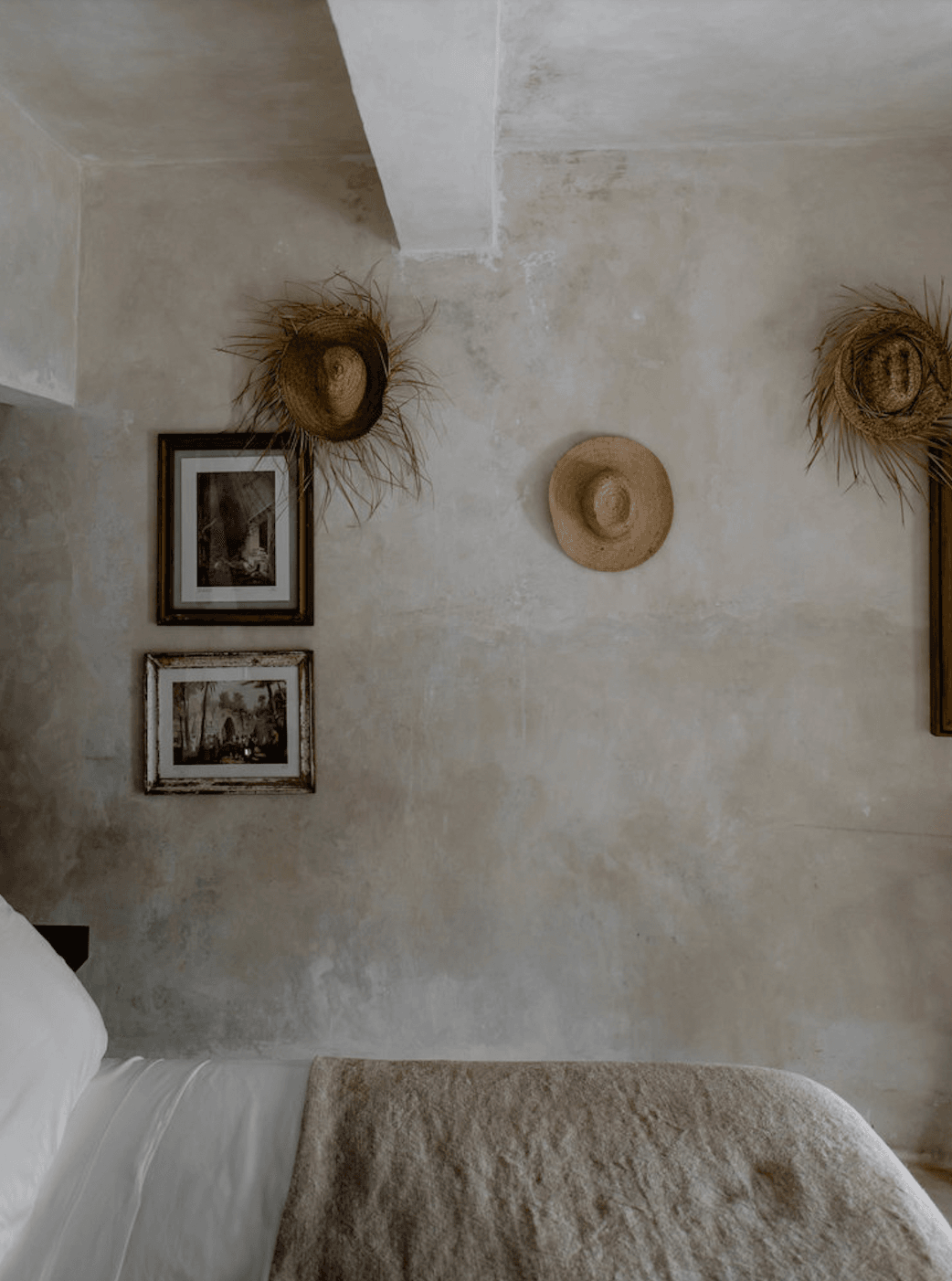 Coqui Coqui Papholchac, Mexico — Minimalist bedroom with whitewashed walls, straw hats, framed photographs, and natural linen bedding creating serene rustic luxury.