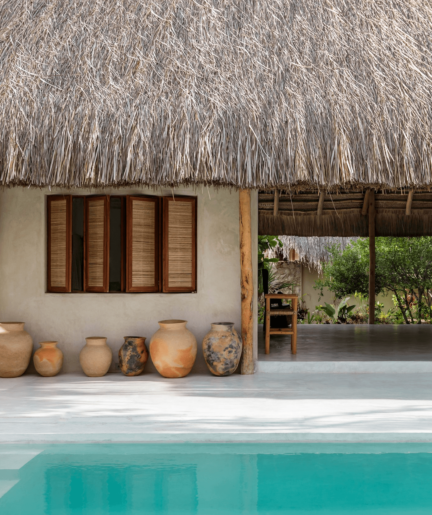 Sussurro, Africa — Thatched-roof pavilion with terra-cotta vessels, wooden louvered windows, and turquoise pool reflecting minimalist tropical design.