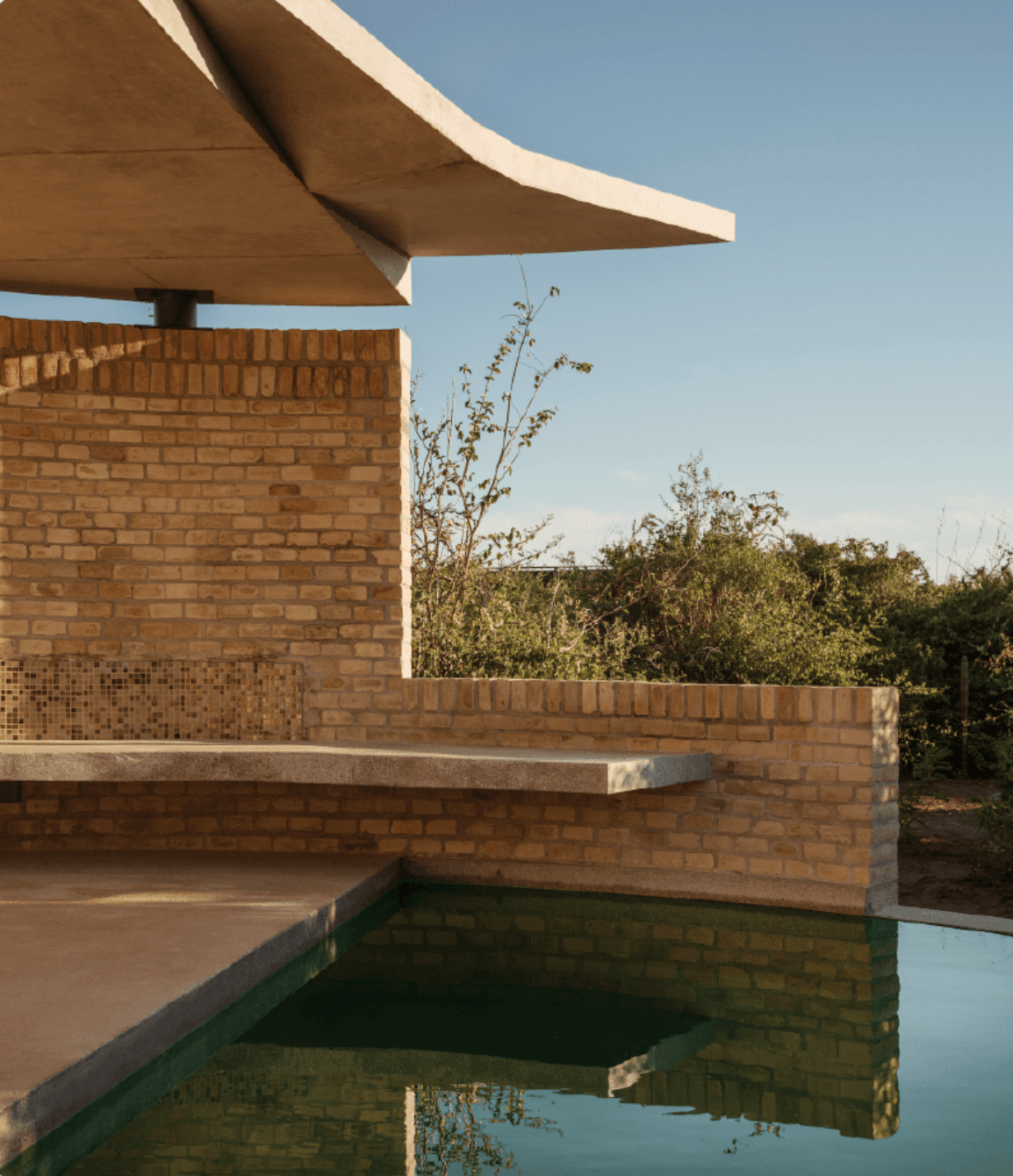 Hotel Terrestre, Mexico — Brick pavilion with curved concrete canopy overlooking still water, modernist architecture amid desert landscape.