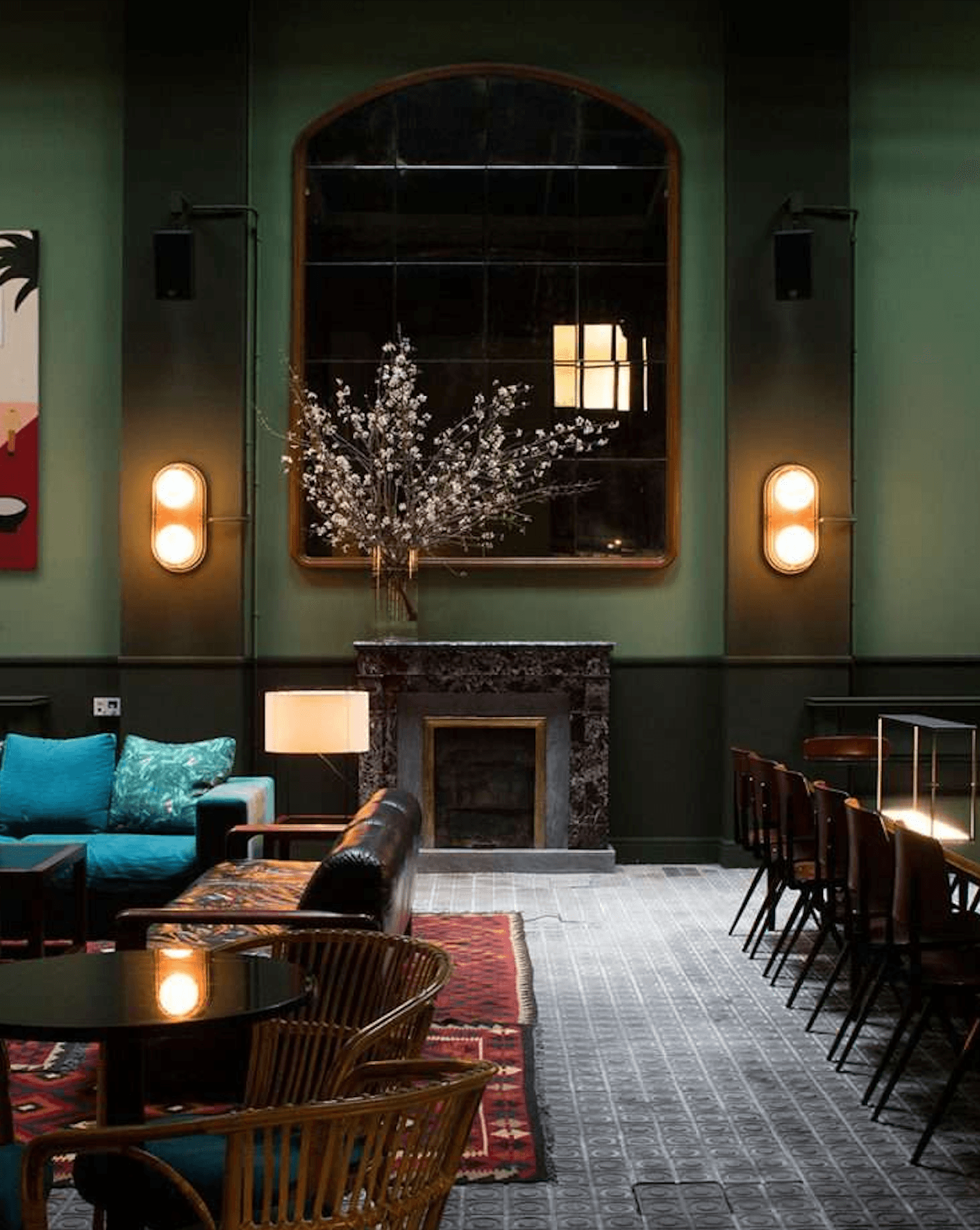 Casa Bonay, Europe — Sage-green lounge with arched mirror, marble fireplace, brass sconces, and modernist seating arranged around glowing pendant lights.