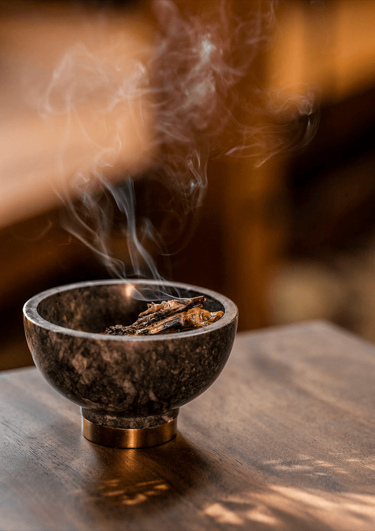One&Only Mandarina, Mexico — Stone incense bowl with brass base releasing aromatic smoke, warm natural light casting shadows on wooden surface, spa and wellness ambiance.
