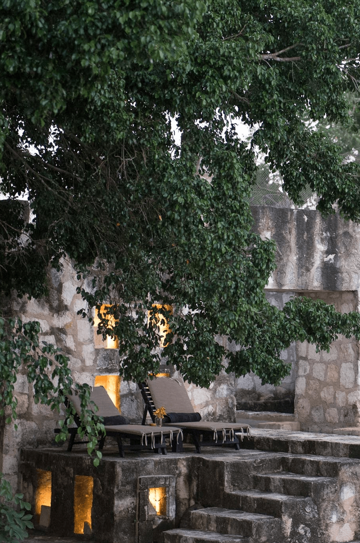 Coqui Coqui Papholchac, Mexico — Stone courtyard with ivy-draped walls, loungers, and warm golden light from arched alcoves at dusk.