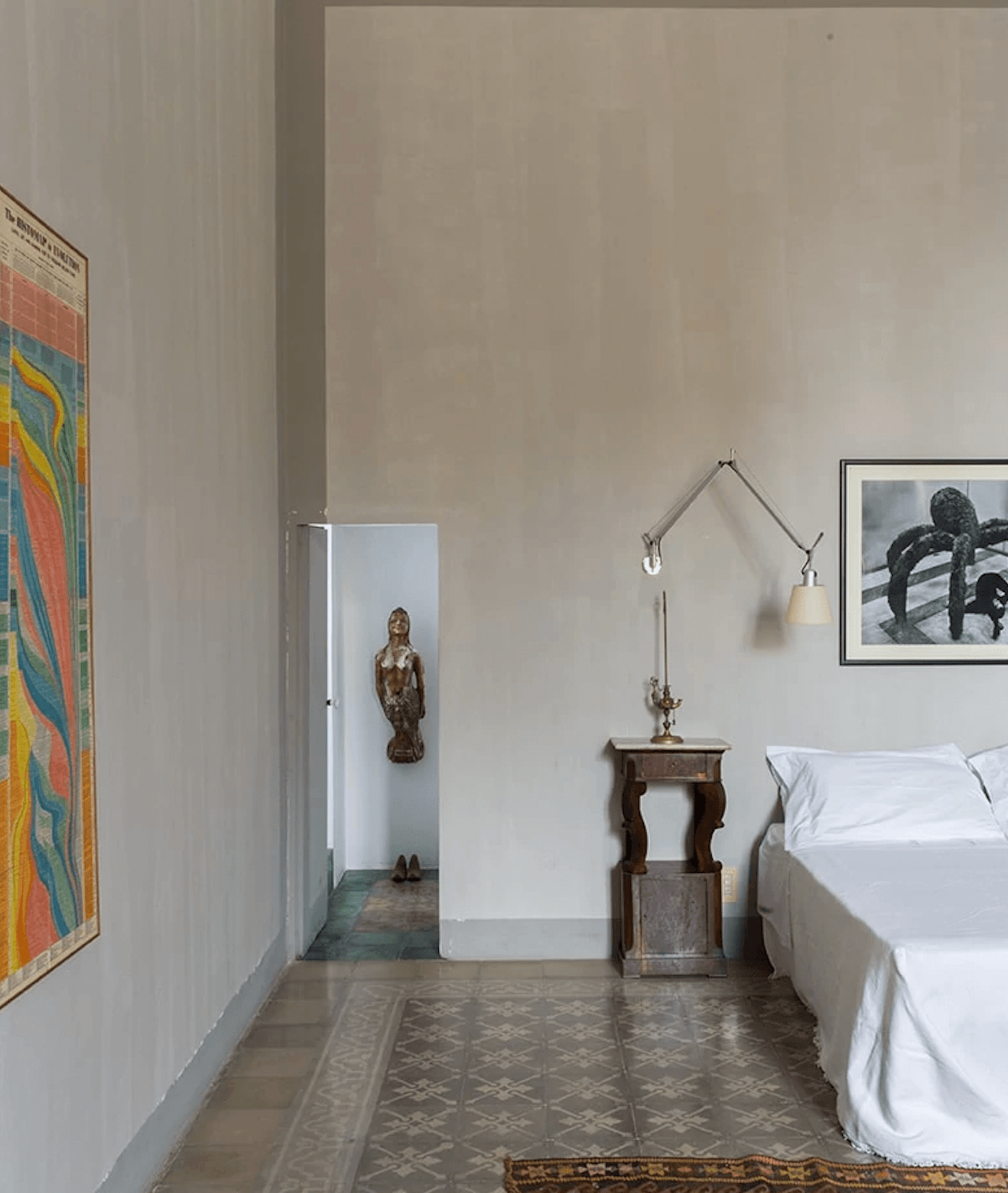 Palazzo Daniele, Europe — Minimalist bedroom gallery with terracotta tile floors, wooden side table, brass sconces, framed photographs, and sculptural alcove niche.