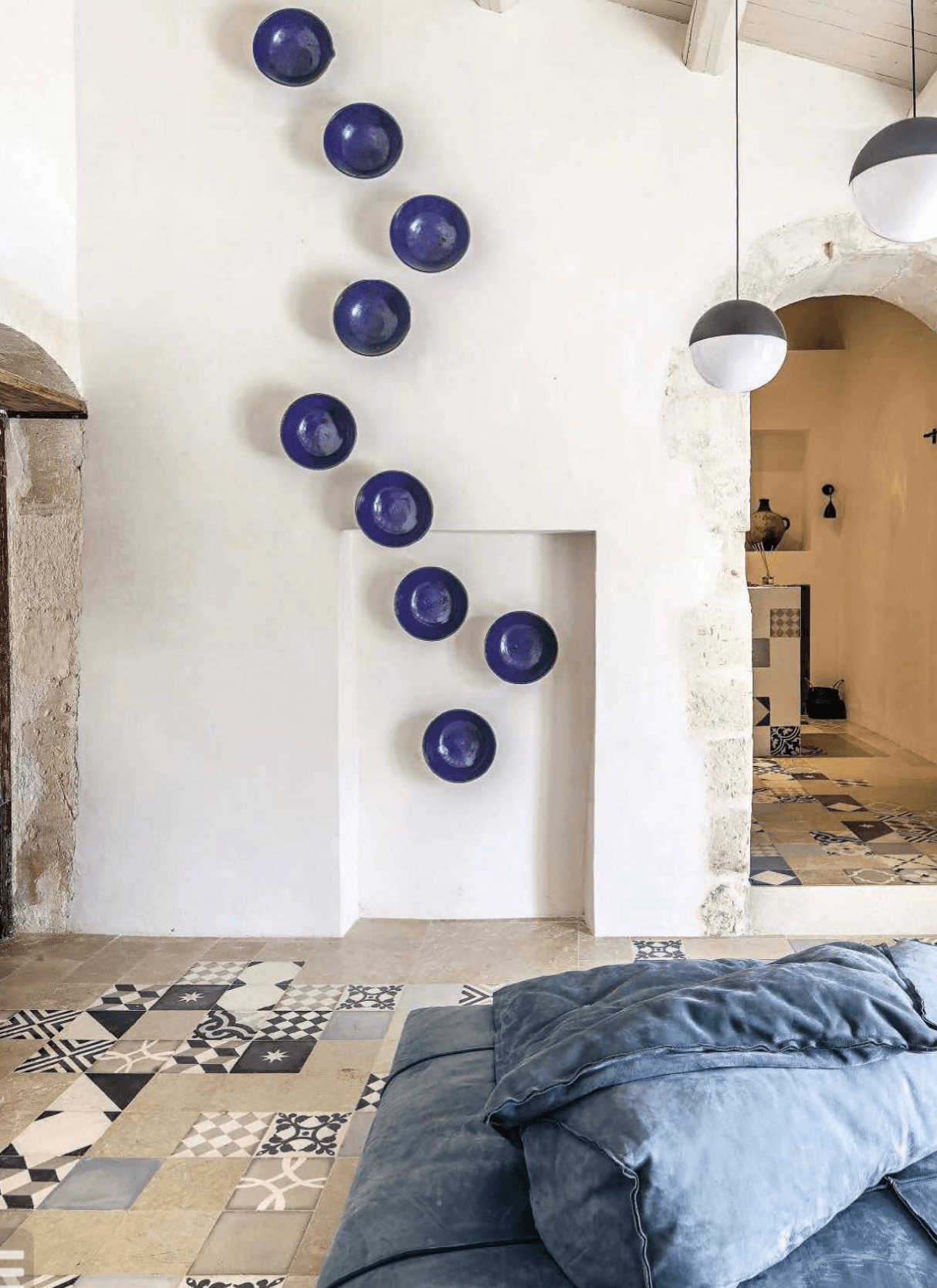 Dimora delle Balze, Europe — White stone archway with nine cobalt ceramic plates arranged vertically, geometric tile flooring, minimalist Mediterranean interior design.