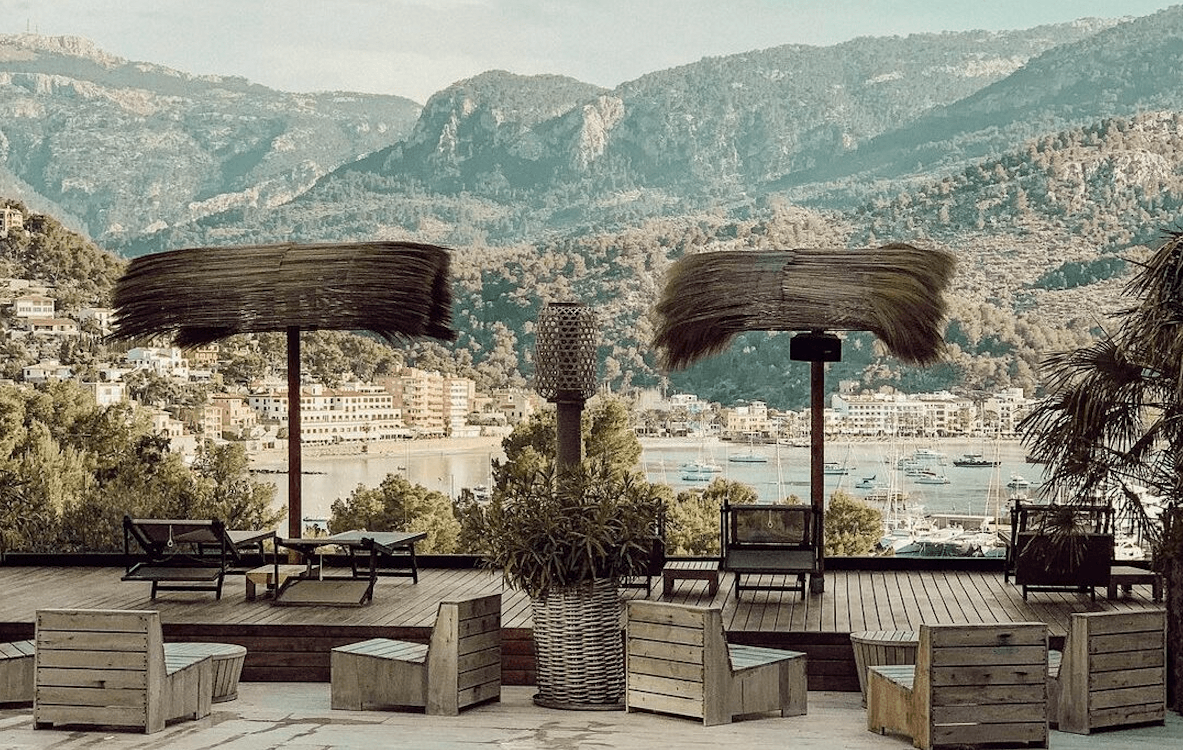 Bikini Hotel, Balearic Islands — Waterfront terrace with dark wooden pergolas, lounge seating, and views of Mediterranean bay and forested mountains.