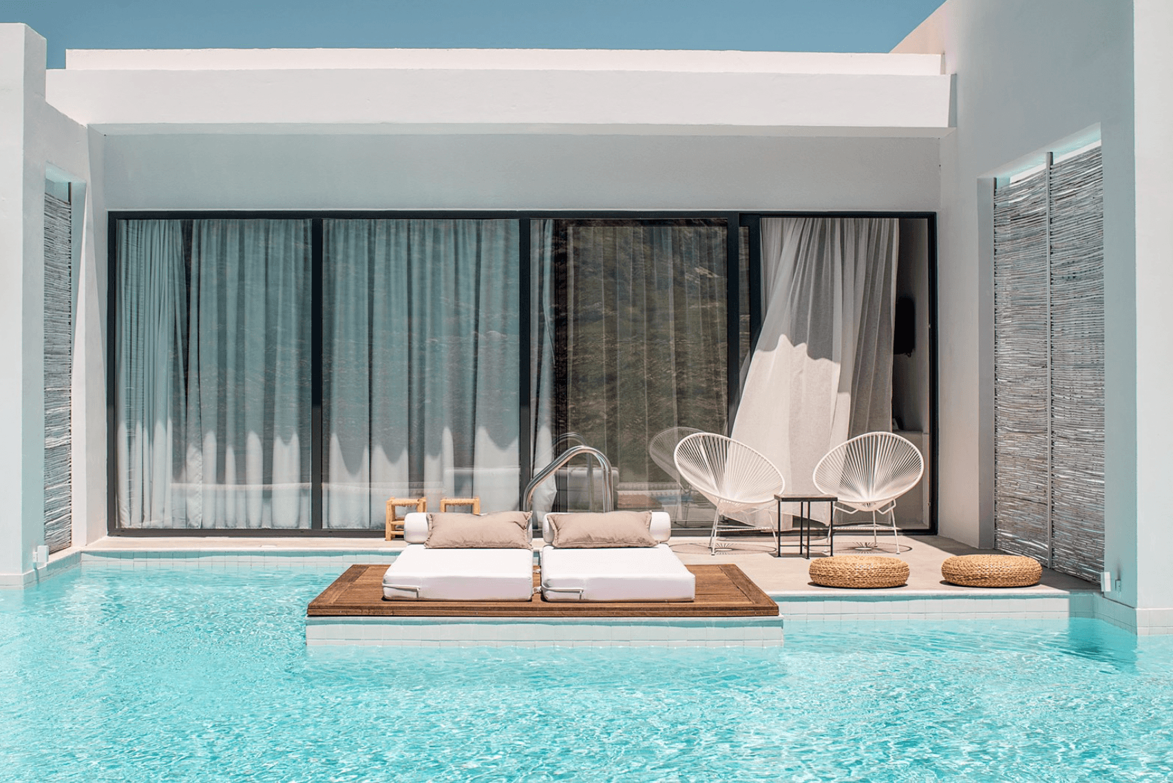 Casa Cook Rhodes, Europe — Minimalist poolside bedroom with turquoise water, wooden platform bed, white curved chairs, floor-to-ceiling windows, neutral linens, natural light.