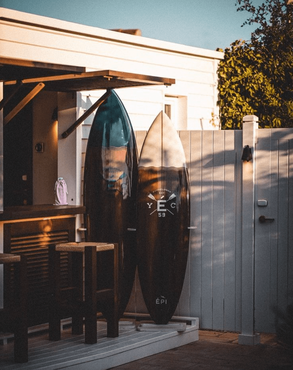 Epi 1959, Europe — Dark surfboards leaning against modern wooden structure, coastal design aesthetic with minimalist architecture and natural light casting shadows on gray fence.