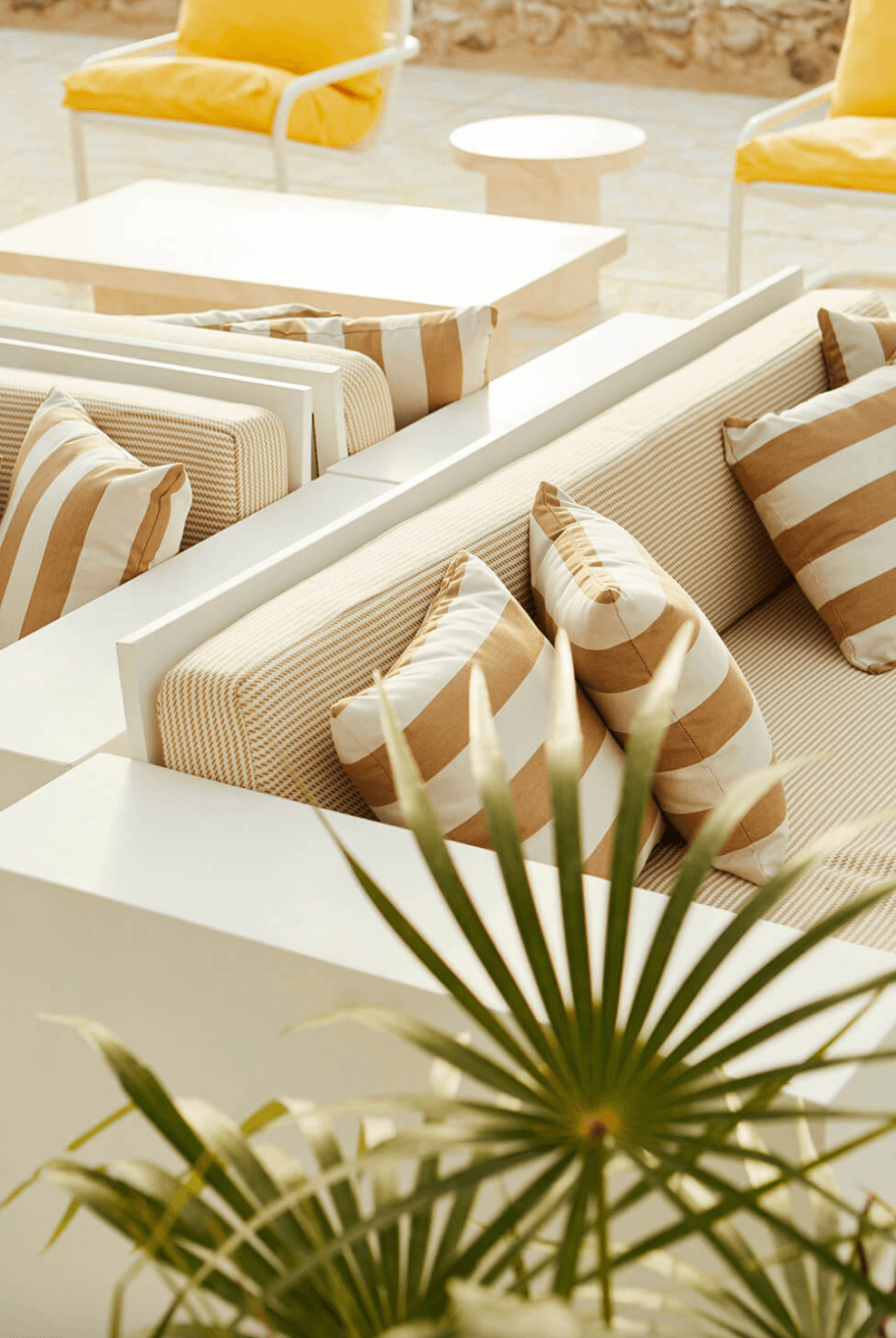 Palm Heights, North America — Minimalist poolside lounge with striped cushions, white tables, natural light, and palm fronds in neutral tones and soft yellow accents.