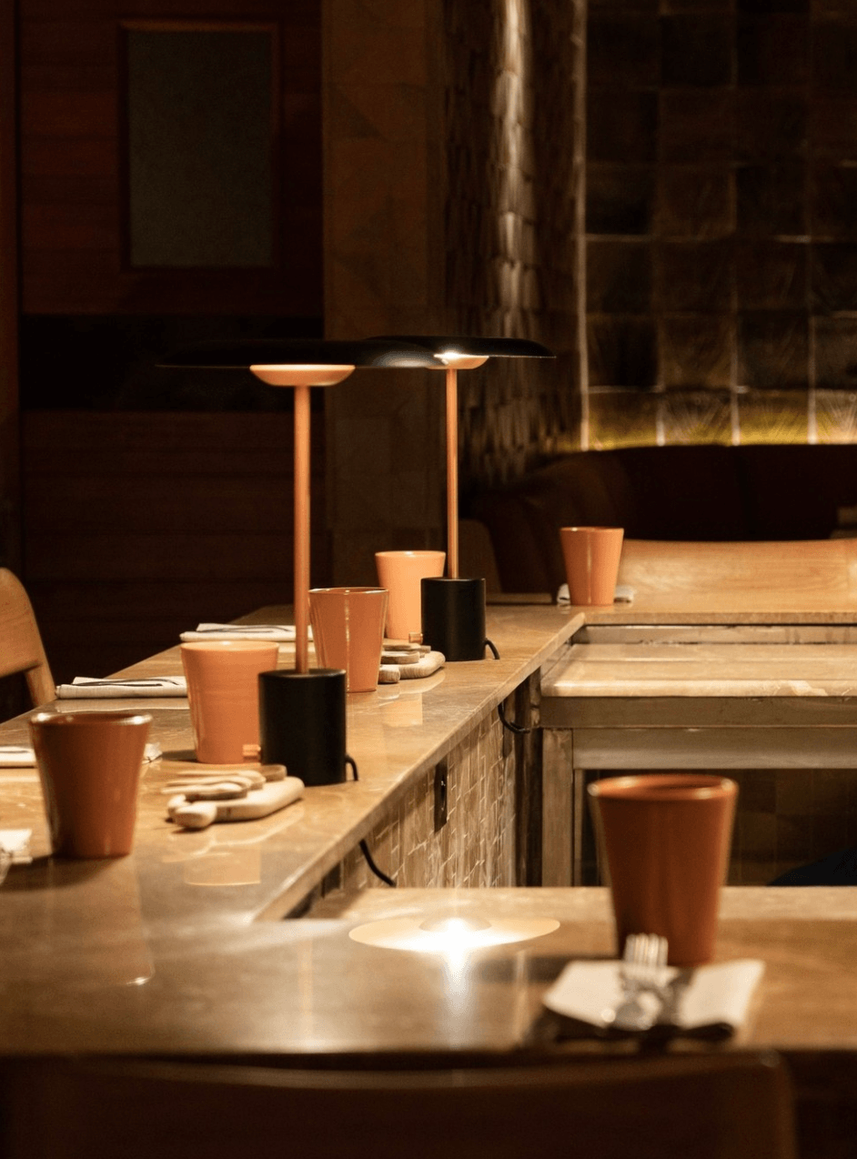 Sahbi Sahbi, Africa — Minimalist restaurant counter with terracotta cups, black pendant lamps, wooden surfaces, and warm ambient lighting overlooking urban architecture.