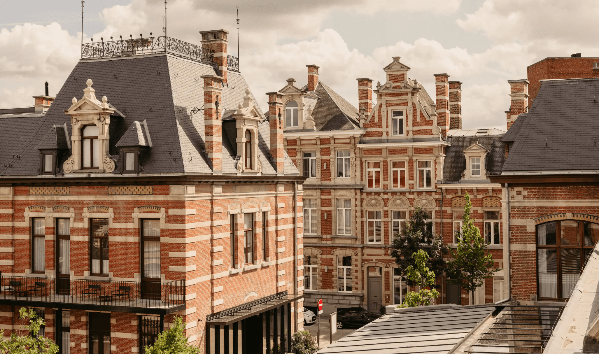 August, Europe — Belle Époque brick mansions with mansard roofs, ornamental chimneys, and cream stone detailing under clouded sky.