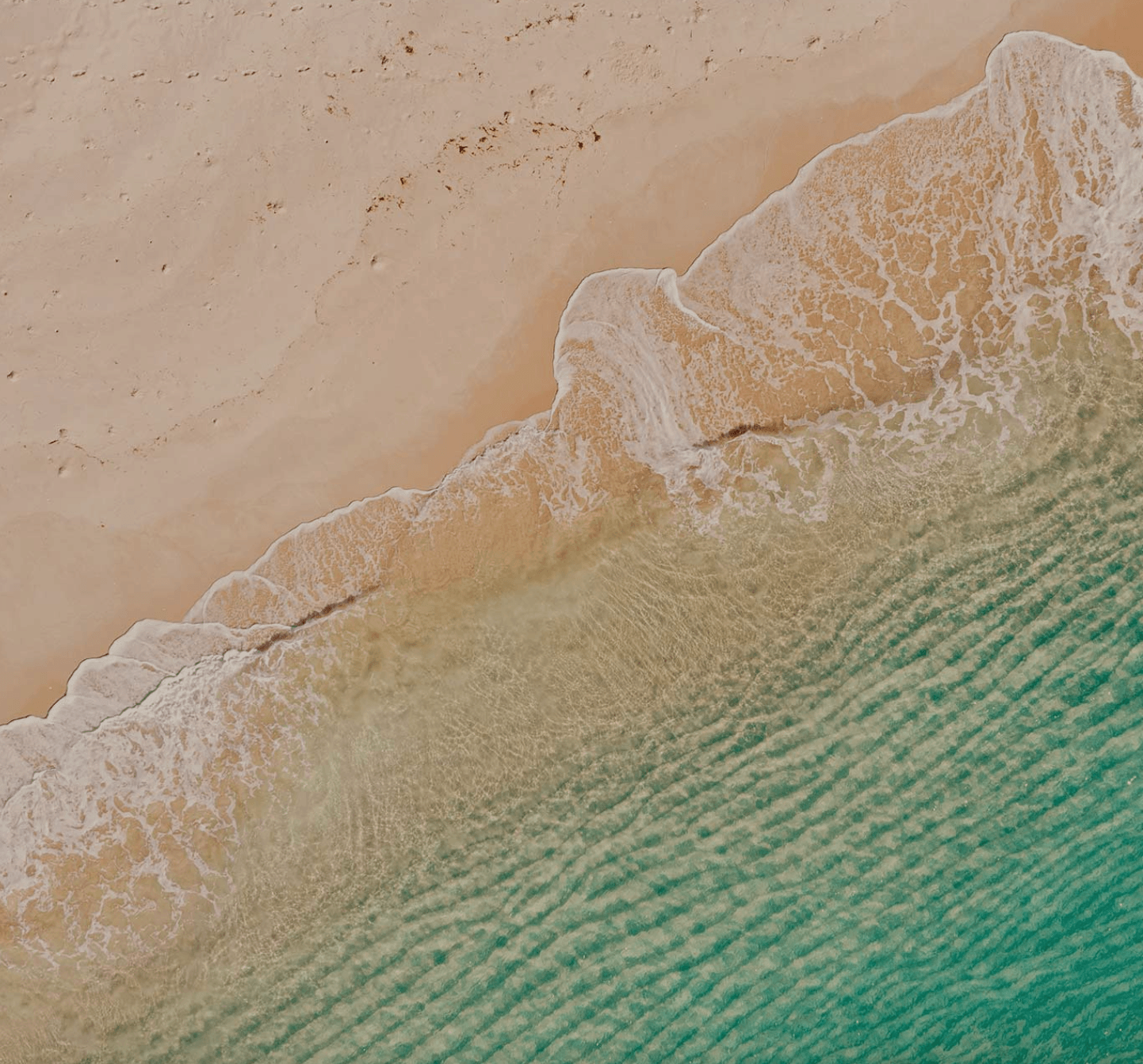 Bazaruto Beach Tour — Aerial view of turquoise ocean water meeting white sandy beach with gentle wave patterns and seafoam along the shoreline.