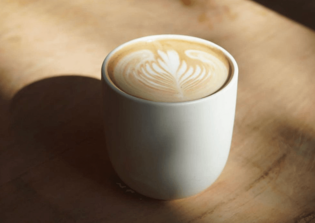 La Cabra Iluminada, Mexico — Cappuccino with latte art in white ceramic cup on wooden surface, natural light