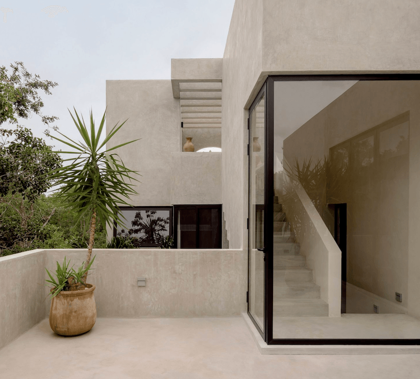 Villa Cava, Mexico — Minimalist concrete terrace with black-framed glass doors, potted palm, and stepped architectural volumes under natural light.