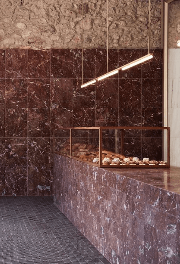 Red Jane, Europe — Luxury spa shower with dark red marble walls, brass linear lighting fixture, and integrated fireplace with river stones.