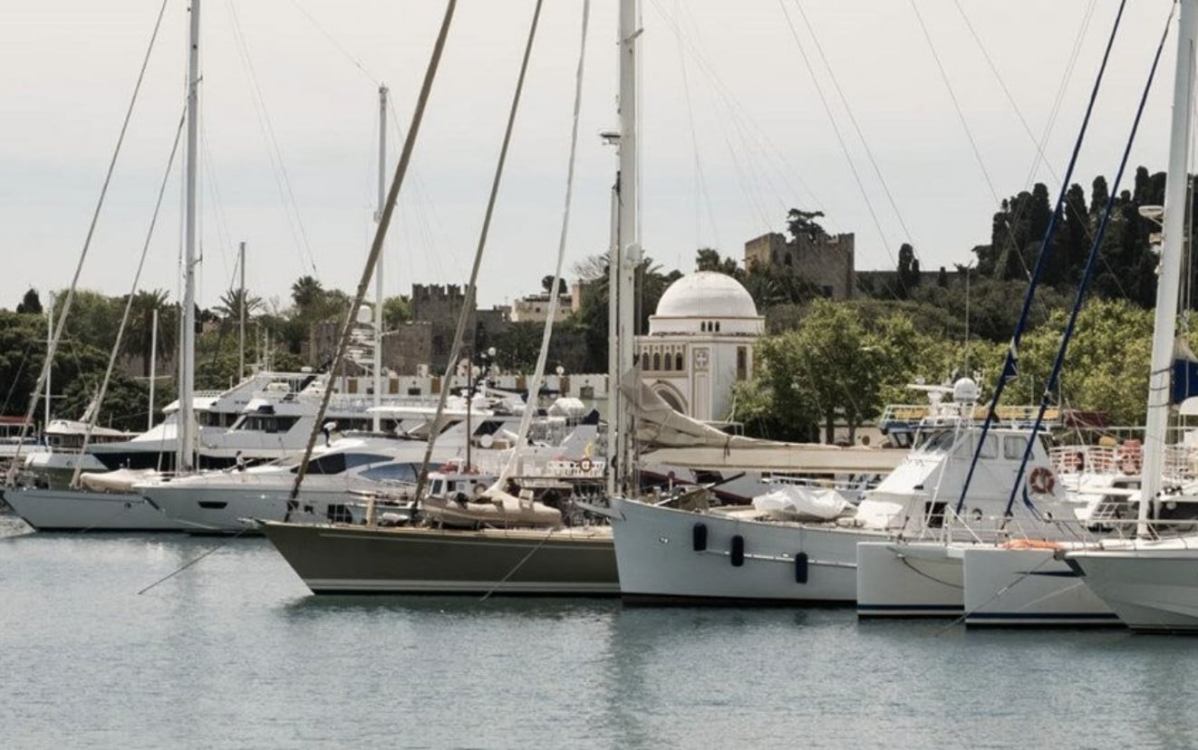 Sail the Coast — Sailboats moored in Mediterranean harbor with white-domed mosque and stone fortifications, coastal European architecture and leisure maritime setting.