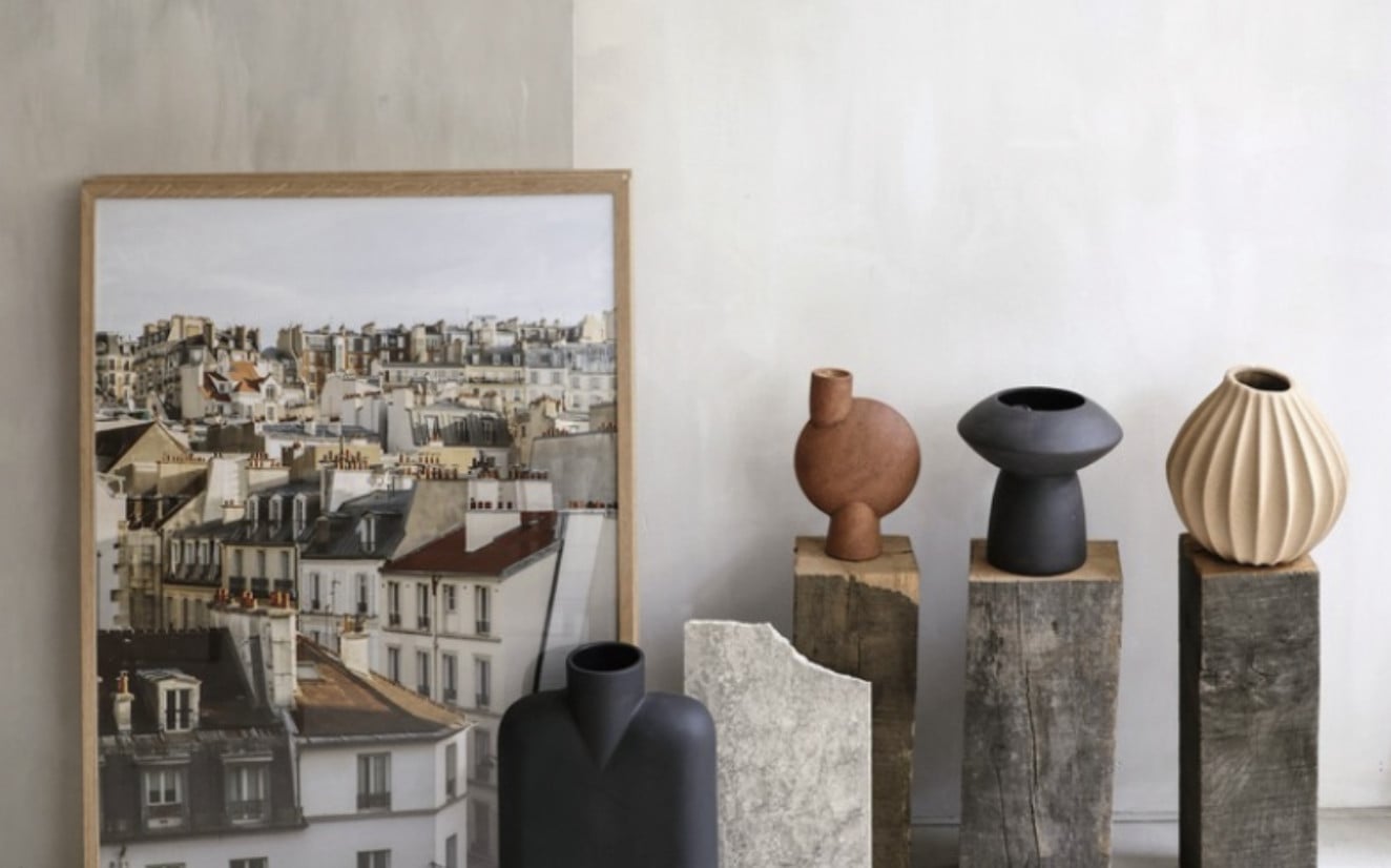 Studio Unfolded, Europe — Ceramic vessels on stone pedestals beside framed Parisian roofscape photograph, minimalist gallery display.