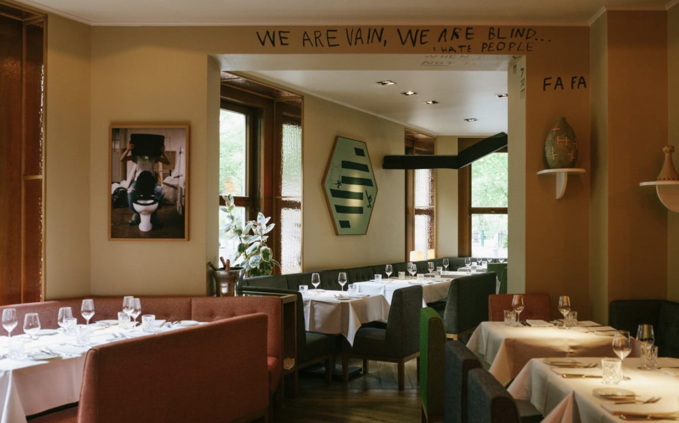 Le Petit Royal, Europe — Dining room with terracotta banquettes, green chairs, white tablecloths, large mirror, and warm ochre walls with contemporary artwork.