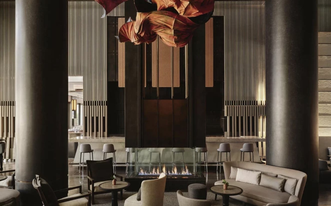 Lounge Bar, North America — Modern fireplace lounge with soaring columns, brass pendant lights, cream seating, and minimalist design aesthetic.