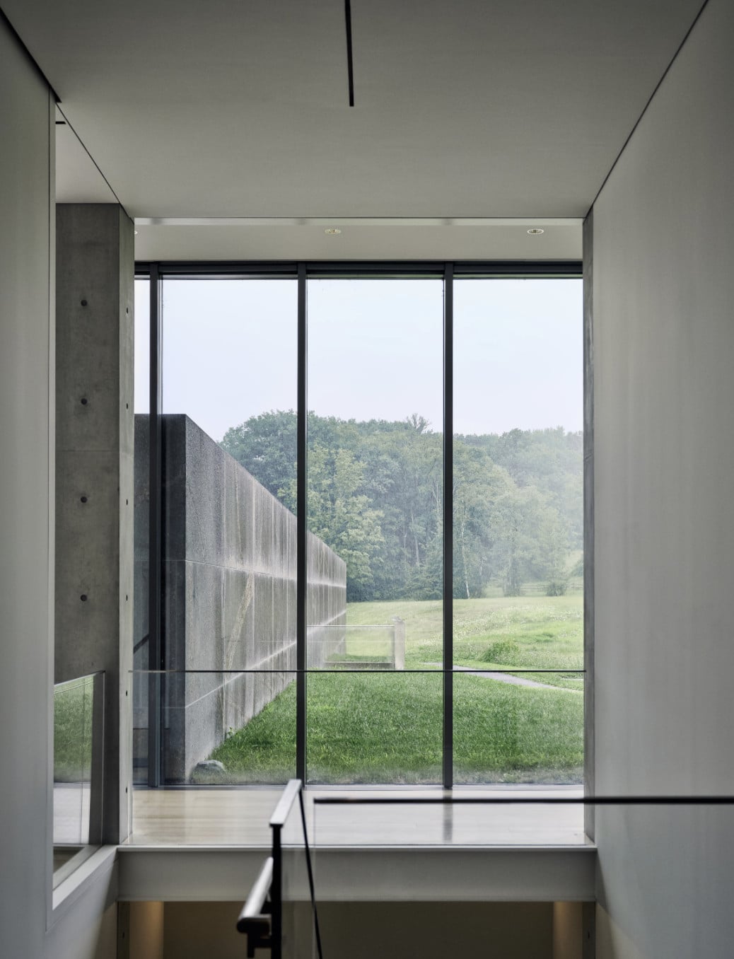 Clark Art Institute — Minimalist interior with floor-to-ceiling windows framing pastoral landscape, concrete structural column, black-framed glazing, natural light flooding neutral gallery space.