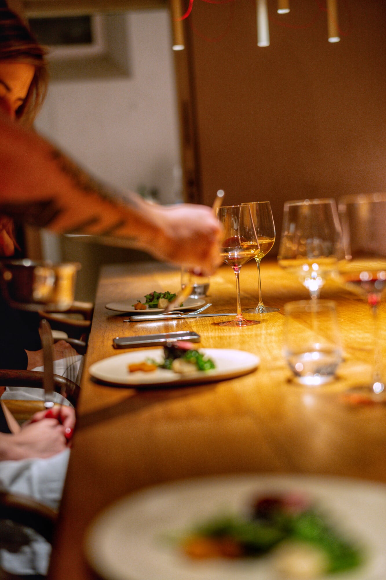 Santa Clara 1728, Portugal — wooden counter dining with wine glasses, plated cuisine, warm ambient lighting, and blurred figures in chef's whites.