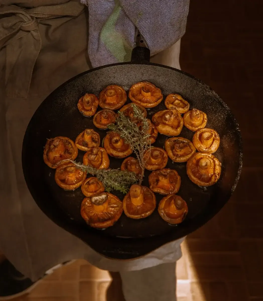 Son Blanc Farmhouse, Balearic Islands — Roasted mushrooms with fresh thyme in cast iron skillet, held by chef in linen apron.