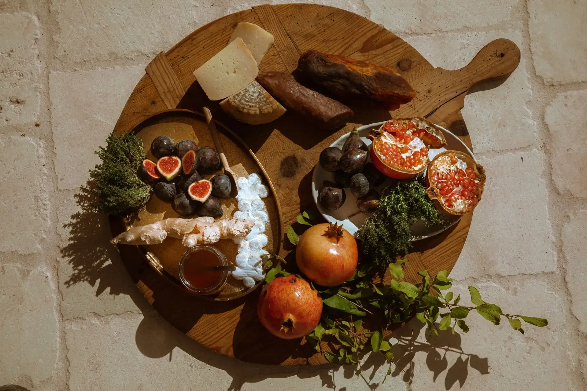 Son Blanc Farmhouse, Balearic Islands, Spain — Wooden board with arranged charcuterie, fresh figs, pomegranates, grapes, cheese, cured meats, sea salt, and fresh herbs in natural light.
