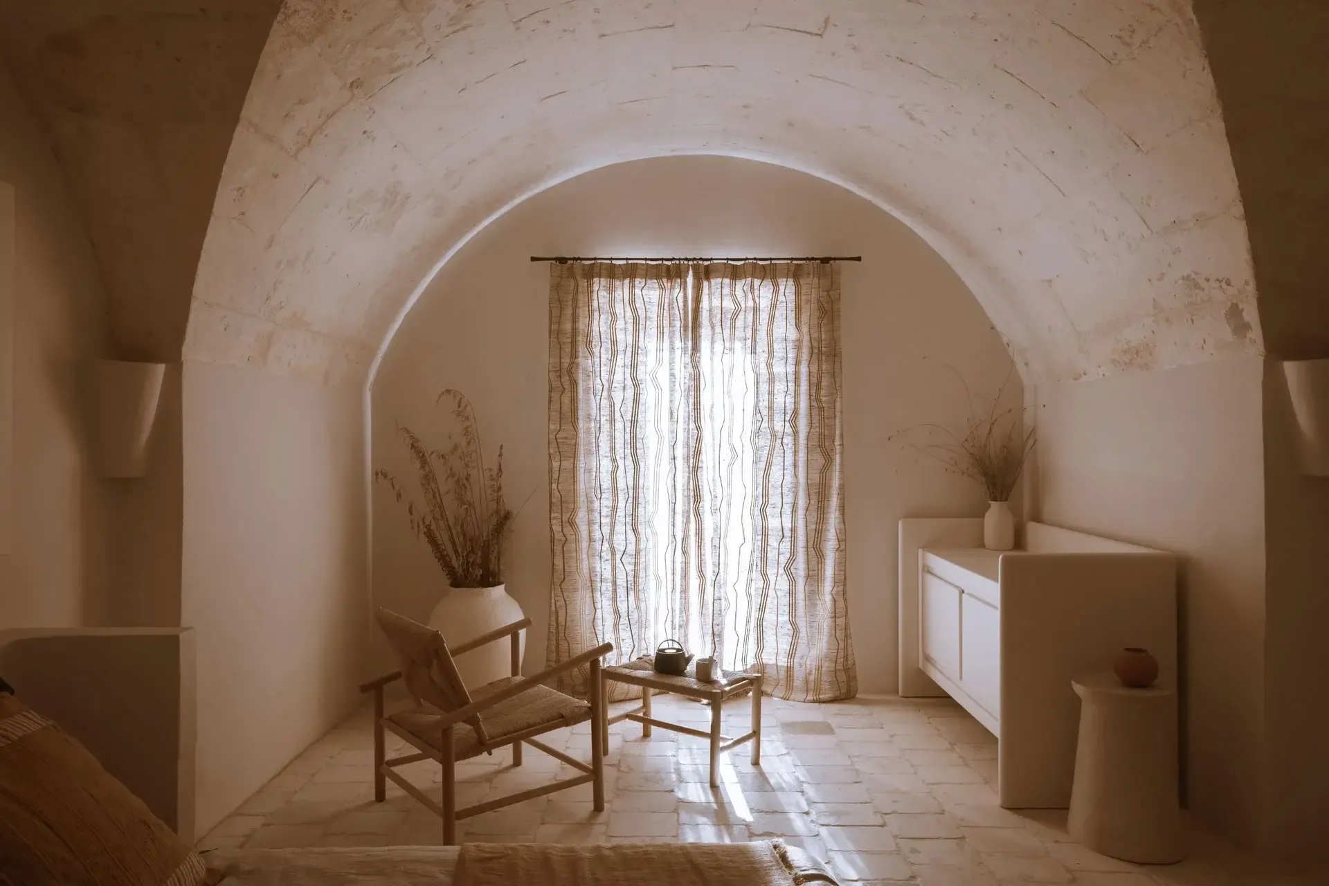 Son Blanc Farmhouse, Balearic Islands, Spain — Arched stone passageway with natural light, wooden chair, linen curtains, minimalist Mediterranean interior design.