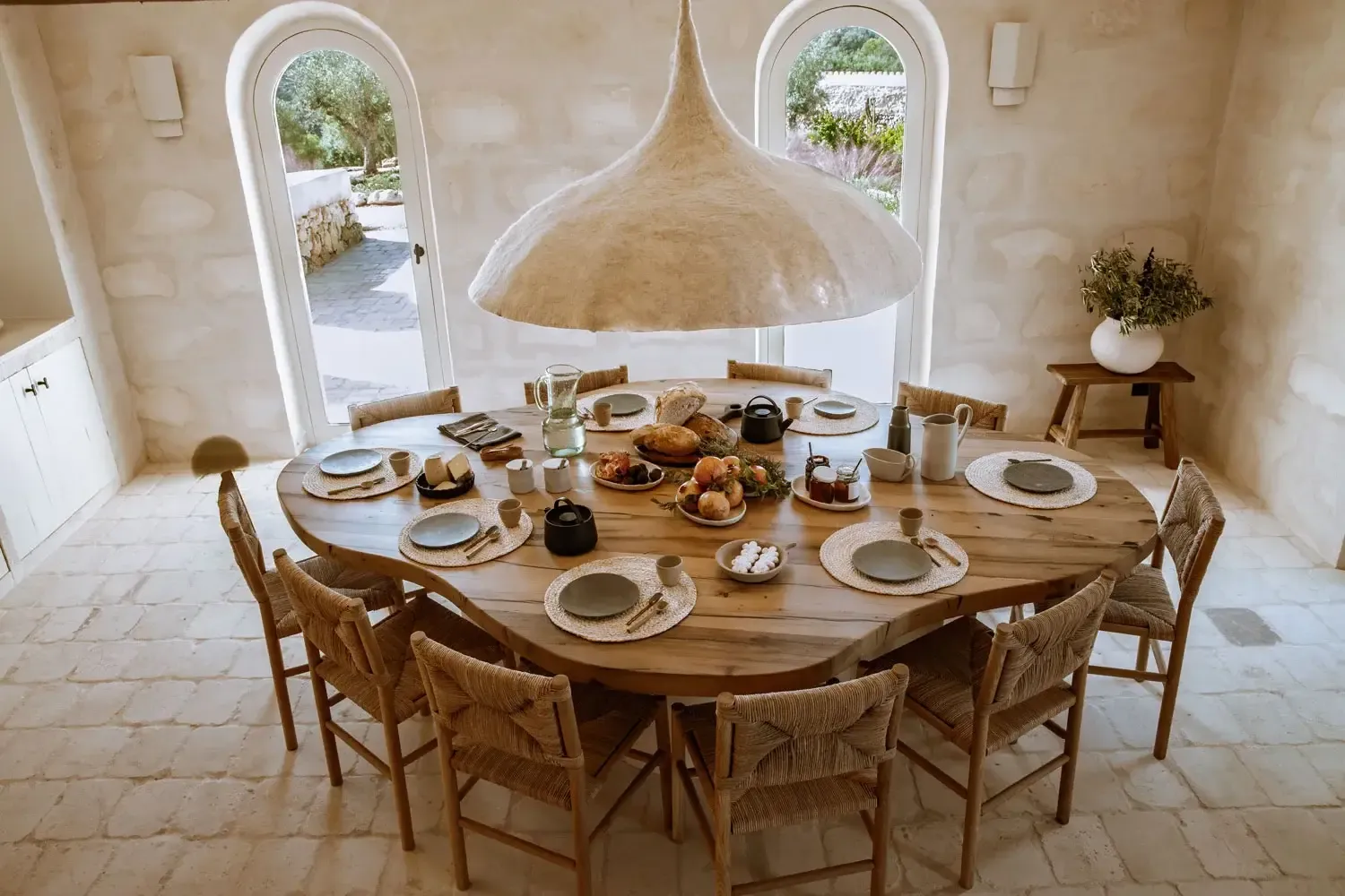 Son Blanc Farmhouse, Balearic Islands, Spain — Whitewashed dining room with domed ceiling, round wooden table, woven chairs, archways opening to Mediterranean landscape.