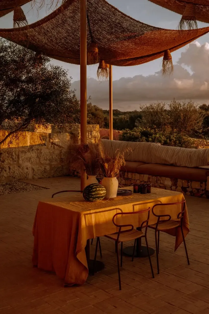 Son Blanc Farmhouse, Balearic Islands — Terracotta table beneath woven canopy at sunset, olive groves and stone walls beyond, Mediterranean luxury hospitality design.